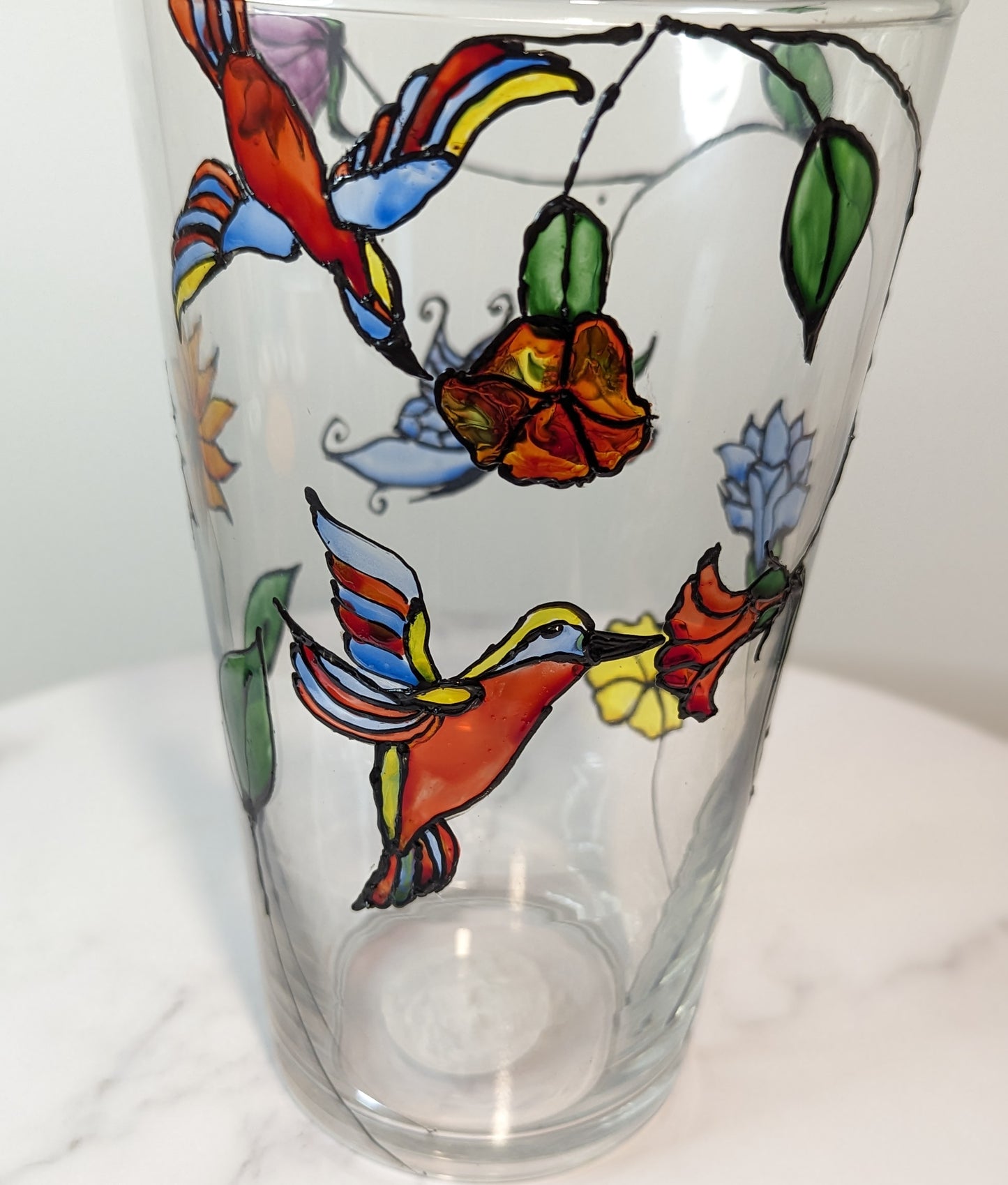 Personalised hand-painted glass vase with colourful parrots, flowers and butterflies.This hand-painted glass vase features a unique depiction of flying parrots surrounded by vibrant flowers and butterflies, capturing the essence of colourful nature and jo