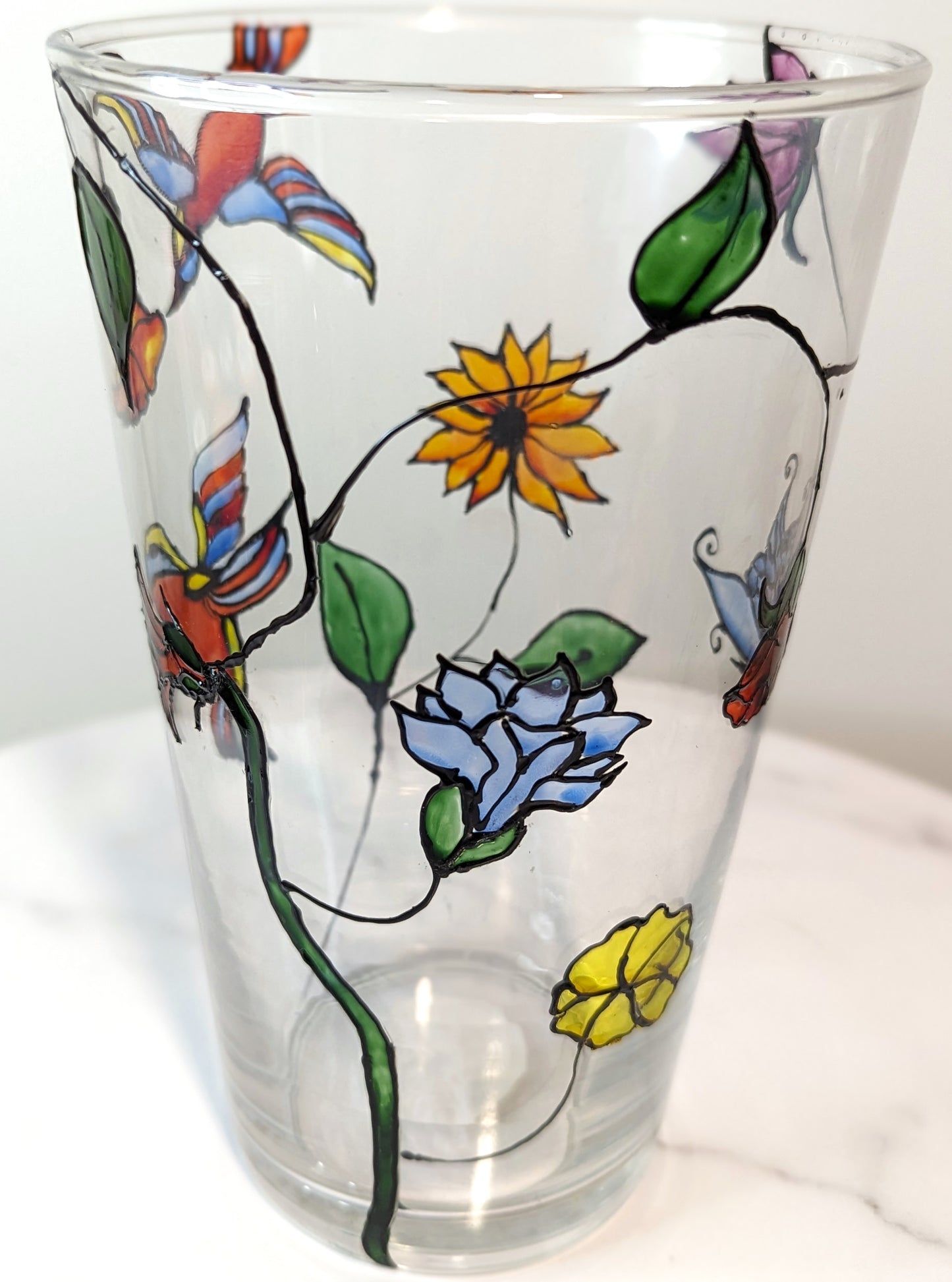 Personalised hand-painted glass vase with colourful parrots, flowers and butterflies.This hand-painted glass vase features a unique depiction of flying parrots surrounded by vibrant flowers and butterflies, capturing the essence of colourful nature and jo
